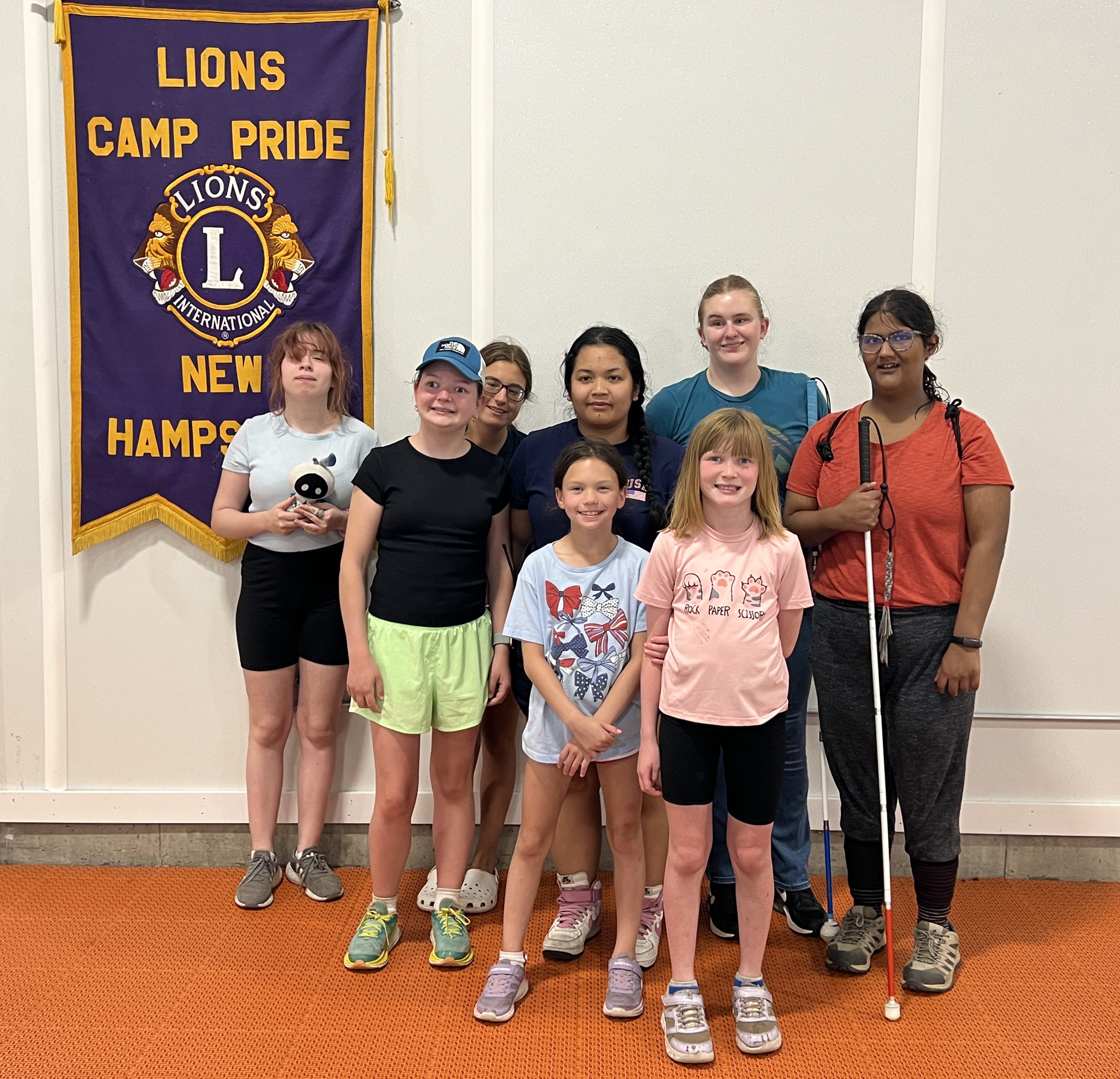 Group of smiling campers stand next to the Lions Club Camp Pride banner.